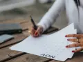 Une main avec des ongles rouges écrit sur un calendrier, planifiant peut-être la date de mariage. Un téléphone et un carnet sont à proximité.