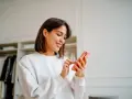 Uśmiechnięta kobieta przegląda telefon w swojej garderobie. Jej gotowy biogram czeka na publikację.