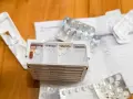 Tablettendose mit Fächern für morgens, mittags, abends, nachts. Leere Blister und ein Medikament liegen daneben.