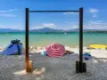Słoneczne plaże nad Jeziorem Garda, z turkusową wodą, górami w tle i kolorowymi parasolami.