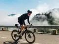 A cyclist in black gear conquers a mountain road, enjoying the breathtaking views and the freedom of long rides amidst swirling clouds.