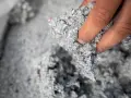 Dłoń trzyma materiał do celuloza ocieplenie. Jest to szara, włóknista masa z kolorowymi drobinkami.