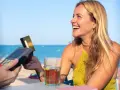 Lachende Frau bezahlt am Strand mit Karte. Selbst mit Krankengeld ist Urlaubsgeld drin!