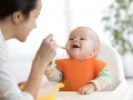 Mama karmi uśmiechniętego niemowlaka łyżeczką. To idealny przykład, co na śniadanie dla niemowlaka – zdrowo i radośnie!
