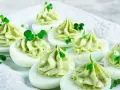 Uova ripiene pasquali, guarnite con crema verde e germogli freschi, pronte per essere gustate.