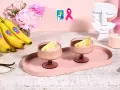Due coppe di cremoso gelato alla banana, guarnite con fettine di banana e cacao, su un vassoio rosa. Banane fresche e fiori rosa sullo sfondo.