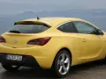 Żółta Astra GTC z tablicą rejestracyjną GG ER 116 stoi na tle morza i gór.