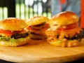 Trzy soczyste burgery z roztopionym serem, pomidorem i sałatą na desce.