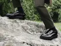 Scarpe oxford derby lucide su una roccia, con pantaloni verdi e sfondo verdeggiante.