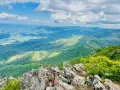 Scenic mountain vista, perfect for day trips from Richmond VA. A winding road snakes through lush green hills under a bright, cloudy sky.