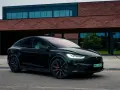 Czarny Tesla Model X zaparkowany przed nowoczesnym budynkiem z cegły.