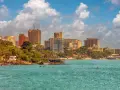 Dakar miasto: nowoczesne budynki i zielone wzgórza nad turkusowym oceanem, łodzie kołyszą się na falach.