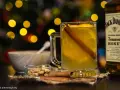Rozgrzewający drink z Jack Daniels Tennessee Honey, z pomarańczą i cynamonem, w blasku świątecznych światełek.