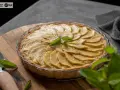 Tarta de manzana casera, con láminas de manzana doradas y una hoja de menta fresca en el centro.