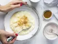 Cremiger Milchreis mit Vanillepudding, bestreut mit Zimt. Eine Hand mit roten Nägeln hält einen Löffel bereit.
