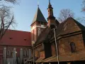 Drewniana i ceglana architektura kościołów w miasteczku śląskim, z wieżą zegarową i strzelistymi dachami, pod błękitnym niebem.