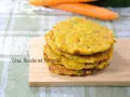 Pancakes dorati di frittata con farina di ceci, serviti su un tagliere di legno, con carote sullo sfondo.