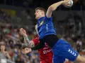 Magnus Landin Jacobsen w skoku do rzutu piłką ręczną, w niebieskim stroju, z widownią w tle.