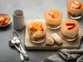 Delizioso tiramisù alle pesche in coppette, con pesche fresche e savoiardi su tagliere di legno.