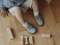 Roczne dziecko bawi się klockami na drewnianej podłodze. Ma na sobie buty z kotkami, idealne do chodzenia po domu.