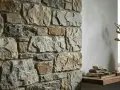 Angolo di un ambiente con un rustico muro in pietra e intonaco, decorato con un vaso e pietre su una mensola.