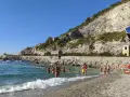 Persone si godono una giornata di sole sulla spiaggia di Erchie, con il mare azzurro e una scogliera imponente alle spalle.