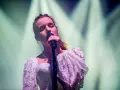 Wokalistka śpiewa z zamkniętymi oczami, w białej, koronkowej sukni. Jej głos rozświetla scenę, jakby rozpraszał szary świat.