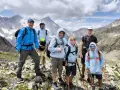 Groupe d'enfants et d'un adulte en randonnée en montagne, souriants, avec des sacs à dos et des bâtons de marche.