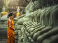 A young monk in orange robes stands before a row of Buddha statues, a scene evoking the ancient roots of what is the oldest religion in the world.