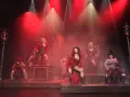 Scena z musicalu "Les Miserables" z kobietami w strojach z epoki, w czerwonym świetle i dymie.