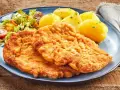 Dwa chrupiące kotlety, jeden sznycel cielęcy, drugi kotlet schabowy, podane z ziemniakami i sałatką.