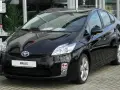 Czarny Toyota Prius 3, hybrydowy samochód, lśni na tle salonu samochodowego.