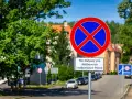 Znak zakaz postoju z tabliczką "Nie dotyczy poj. służbowych i radiowozów Policji" na tle zieleni i zabudowań.