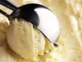 Un cucchiaio raccoglie una pallina di cremoso gelato con yogurt greco, pronto per essere gustato.