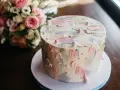 Oto tort na 20 osób, ważący około 2 kg, ozdobiony pastelowymi pociągnięciami pędzla i perełkami. Obok bukiet różowych kwiatów.