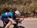 Cyclist pushing hard on a road bike, focused on a VO2 max workout amidst a scenic, tree-lined landscape.