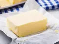 Kostka masła na papierze, obok niebiesko-biała ściereczka. Czy masło można mrozić? Tak, można je zamrozić, by zachować świeżość.