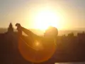 Silhouette d'une personne prenant une photo contre jour avec son téléphone, le soleil éclatant à l'horizon derrière des bâtiments.