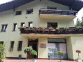 Jasnozielony hotel na błoniach z balkonem pełnym czerwonych kwiatów.