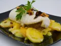 Rape con patatas, un plato delicioso con pescado blanco tierno y patatas doradas, decorado con perejil fresco y crujientes trozos de ajo frito.