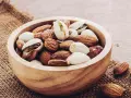Un bol en bois rempli d'amandes et de pistaches, une liste d'oléagineux parfaite pour une collation saine.
