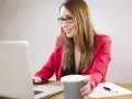 Uśmiechnięta kobieta w okularach pracuje przy laptopie, zastanawiając się, czy można dokupić AC do ubezpieczenia.