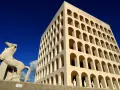 Le palais de la civilisation italienne, monument emblématique, se dresse fièrement sous un ciel bleu éclatant, avec une statue de cheval en avant-plan.