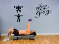 Kvinna tränar med en lila hantel på en stepbräda. Väggen har texten "Keep Going" och silhuetter av styrkelyft.