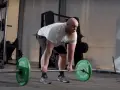 Man med skägg utför raka marklyft med hantlar i ett gym.
