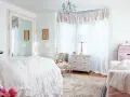 Dormitorio con cama blanca y volantes, espejo grande, cómoda antigua y sillón. Estilo shabby chic.