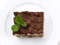 Pyszne tiramisu bez alkoholu, posypane kakao i udekorowane listkami mięty, na białym talerzu.