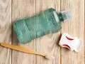 Butelka płynu do płukania ust, nić dentystyczna i bambusowa szczoteczka do zębów na drewnianym tle.
