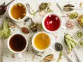 Tasses de tisanes aux herbes variées, idéales pour une infusion douleur règles. Des cuillères regorgent de fleurs séchées et de feuilles.