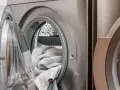 Eine offene Waschmaschine mit einem grauen Handtuch darin. Die Tür ist leicht geöffnet, um die Wäsche nach dem Waschen trocknen zu lassen.